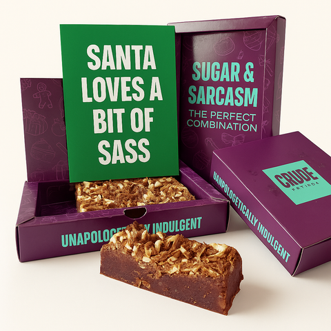 Purple Crude Crumbs brownie gift box opened to reveal a chocolate brownie slab topped with flakes, with a green postcard propped inside reading ‘Santa Loves a Bit of Sass’ in white Zuume Rough font.