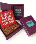 Crude Crumbs purple brownie gift box opened to reveal a chocolate brownie slab, with a red postcard on top reading ‘If Santa Asks We Have Both Been Very Good’ in white Zuume Rough font