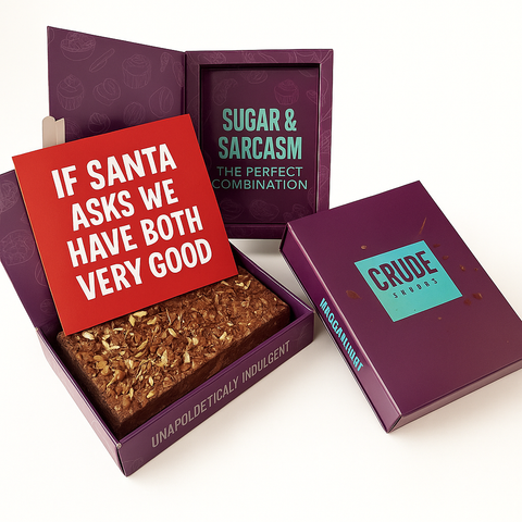 Crude Crumbs purple brownie gift box opened to reveal a chocolate brownie slab, with a red postcard on top reading ‘If Santa Asks We Have Both Been Very Good’ in white Zuume Rough font